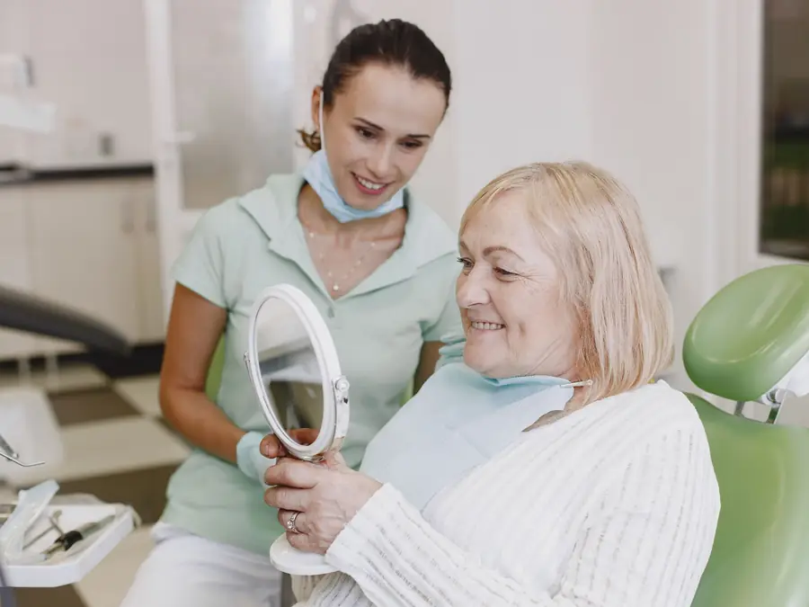 Pacientă privindu-și zâmbetul în oglindă, alături de medic